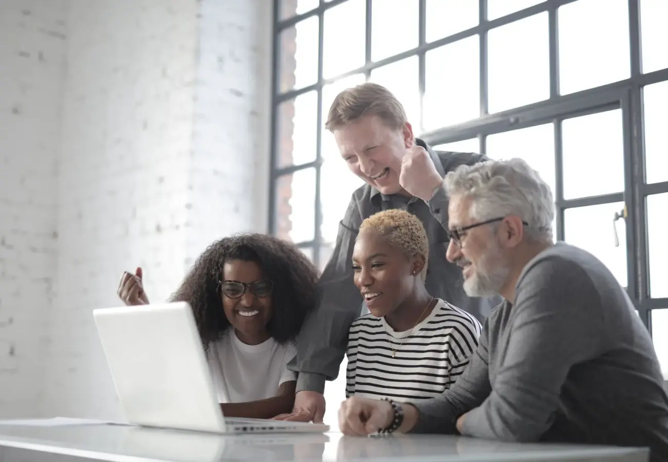 Coworkers talking around a laptop in a bright office